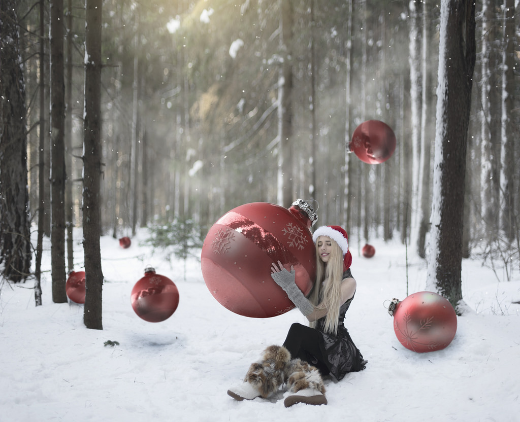 Фото Девушка в новогоднем колпаке, с огромным красным шариком в руках, сидит на снегу