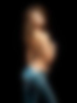 Фото Модель Ирина Шейк / Irina Sheik полуобнаженная в джинсах стоит спиной, прикрыв грудь рукой в перчатке на черном фоне
