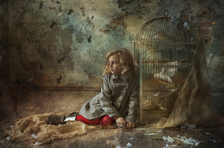 Фото Девочка сидит на полу в разрушенном помещении рядом клетка с голубем
