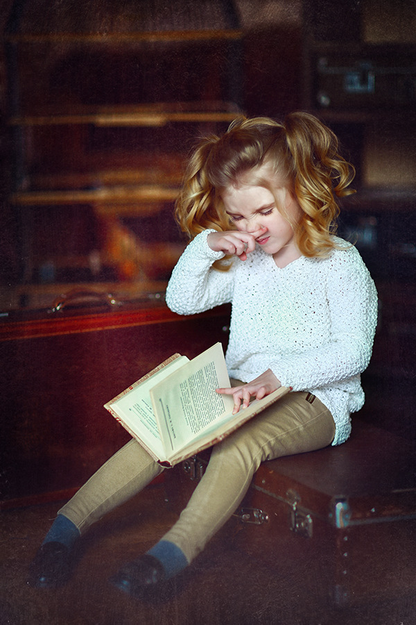 Фото Девочка маленькая с хвостиками, сидя на чемодане, утирая носик свой, листает книгу. Фотограф Наталья Законова
