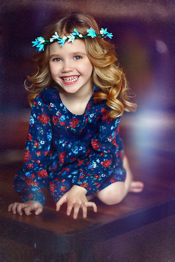 Фото Девочка маленькая красивая голубоглазая с венком и колокольчиков на голове, радостно улыбаясь, сидит на столе. Фотограф Наталья Законова