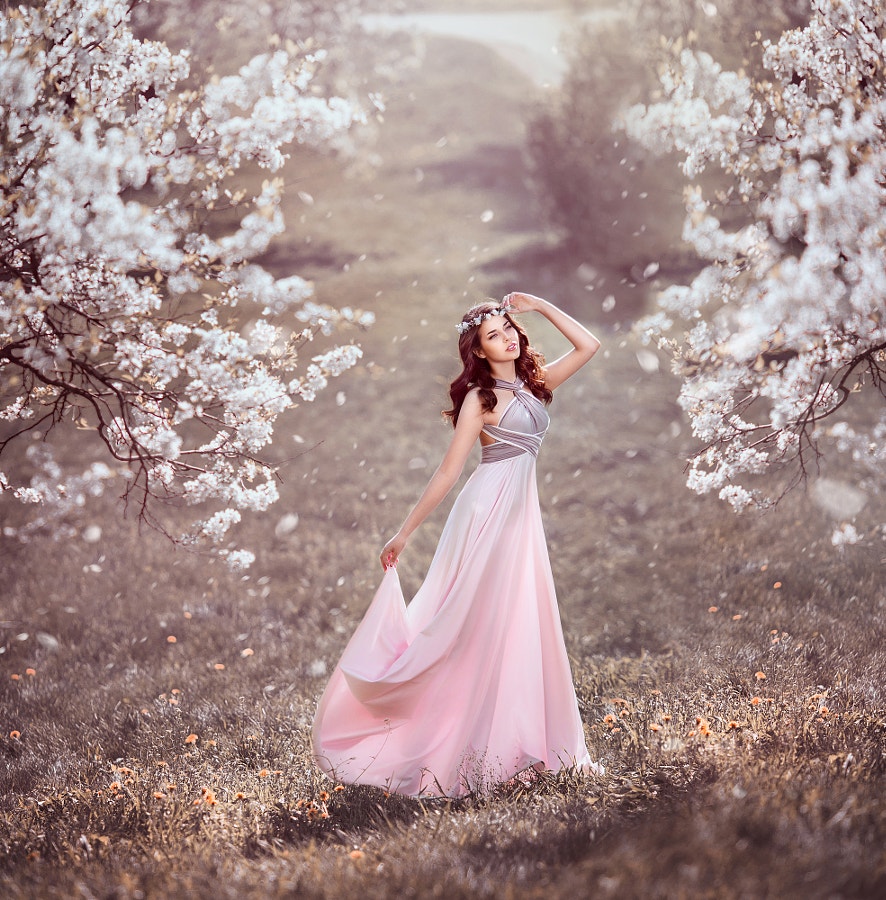Фото Девушка красивая с венком на голове из цветов в легком длинном платье  в благоухающем цветущем саду
