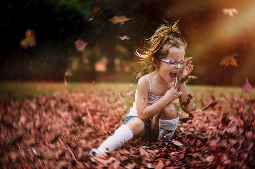 Фото Девочка с закрытыми глазами в очках сидит на осенней листве, которая вихрем кружит вокруг нее