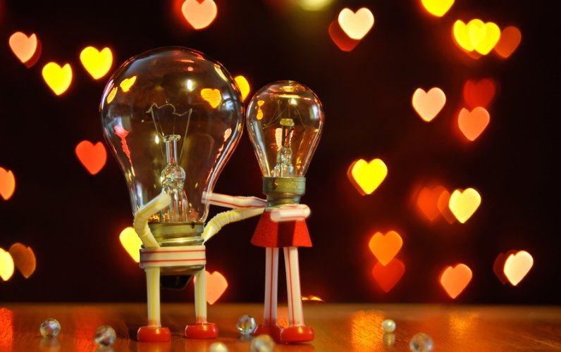 Фото Две лампочки обнимают друг друга, олицетворяя влюбленную пару, а вокруг падают сердечки