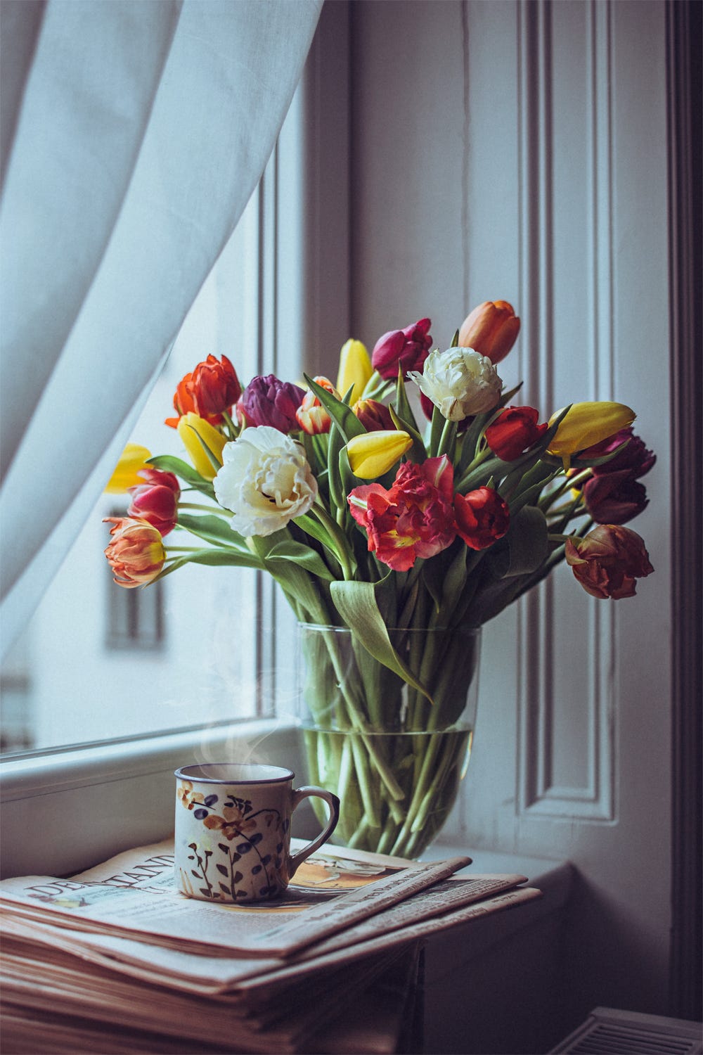 Фото Букет тюльпанов в вазе с водой и чашка горячего чая стоят у окна, фотограф Julia D&;vila-Lampe