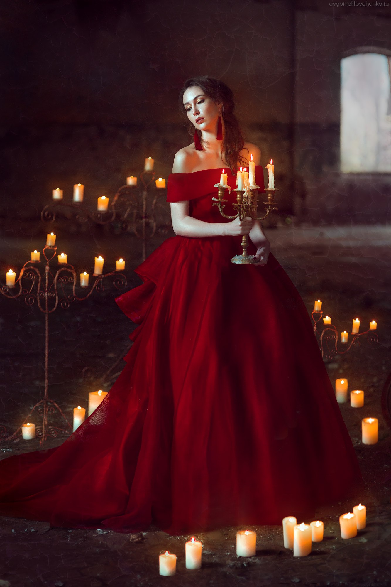 Фото Девушка в красном платье стоит в старом помещении в окружении свечей, держа в руках канделябр. Фотограф Евгения Литовченко / Evgeniya Litovchenko
