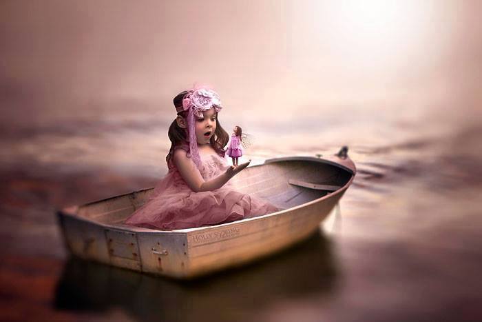 Фото Маленькая девочка, сидящая в лодке, держит девочку - мотылька на руке и удивленно смотрит на нее