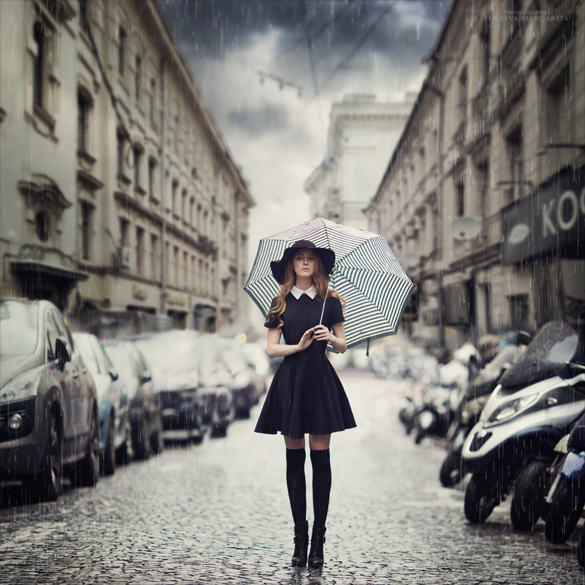 Фото Девушка в темном платье, в шляпе, с зонтом, стоит под дождем, на фоне городского переулка, by Margarita Kareva