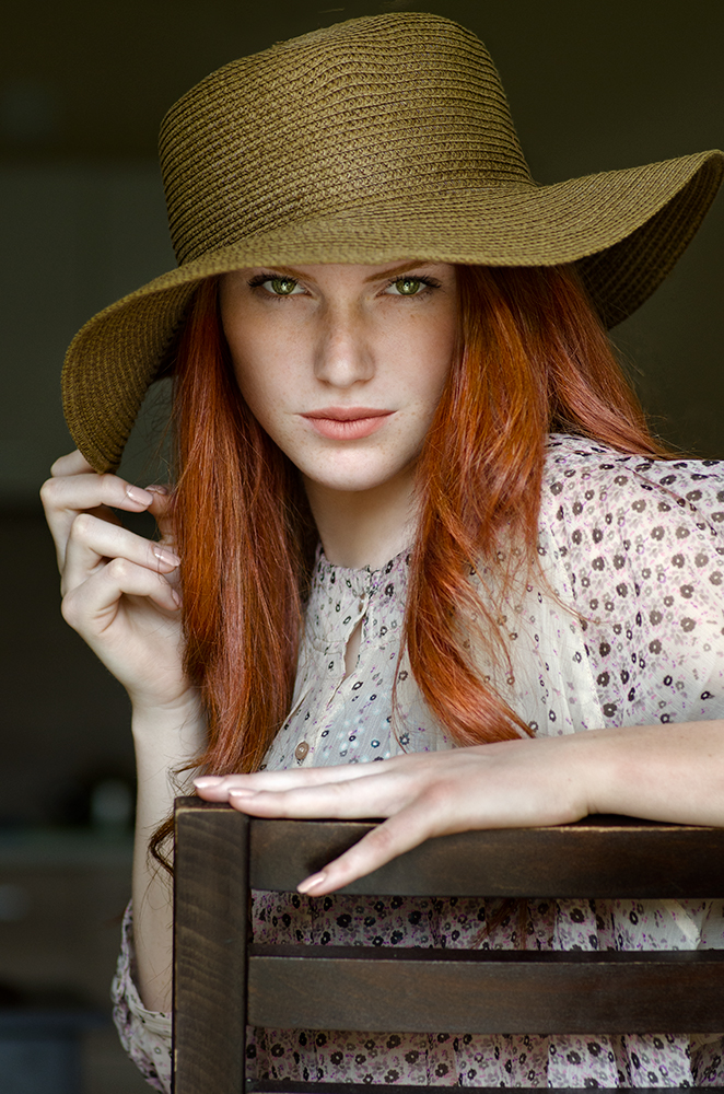 Фото Рыжеволосая девушка в широкополой шляпе, с пронзительным взглядом сидит на стуле. Фотограф Таня Маркова