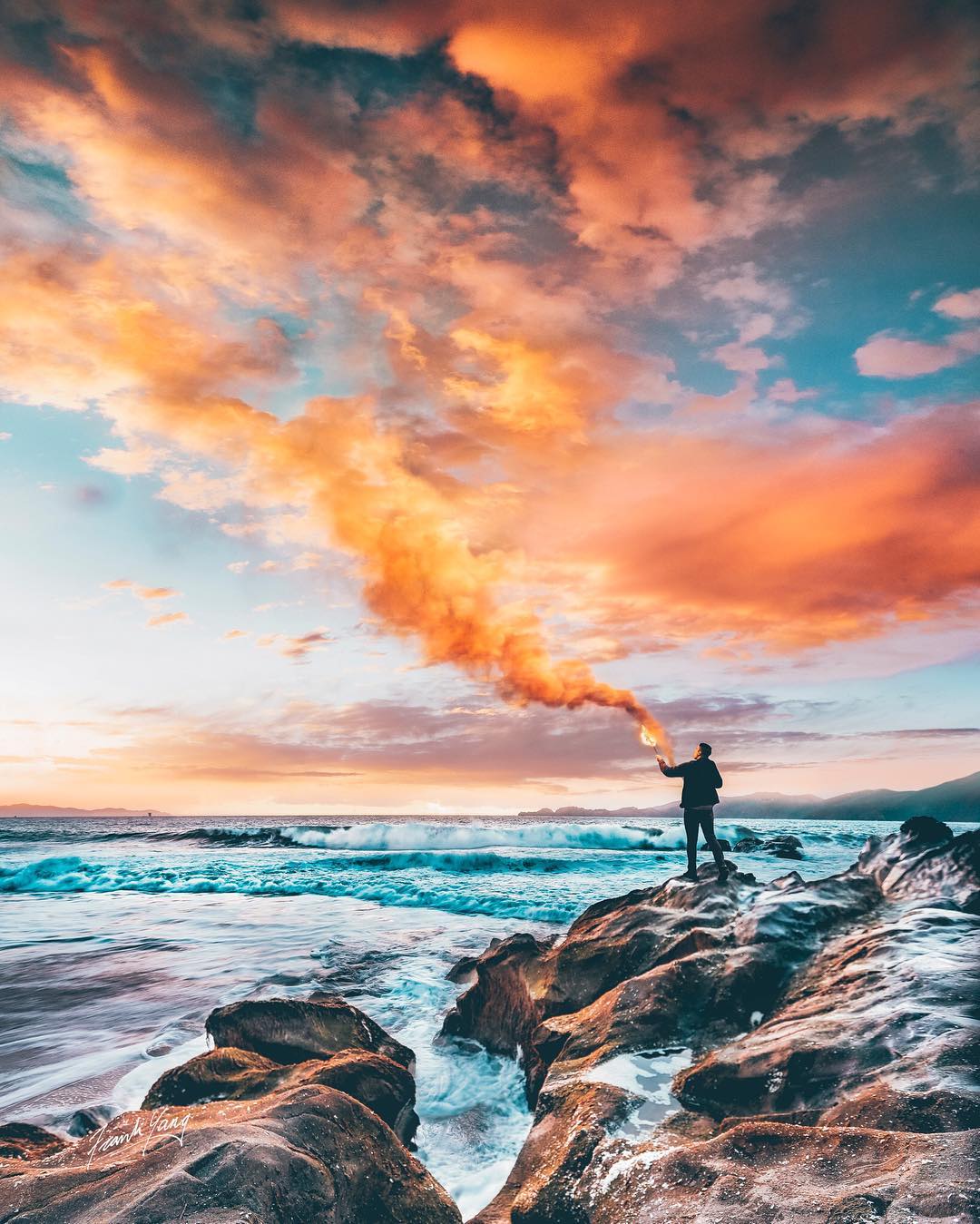Фото Парень с дымовой шашкой стоит на каменистом берегу моря