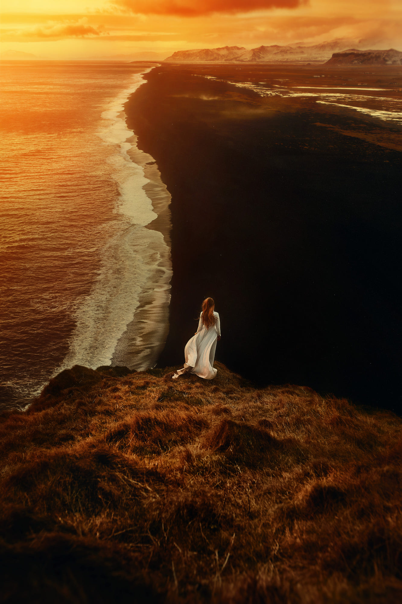 Фото Рыжеволосая девушка в длинном белом платье стоит на обрыве у моря на закате, фотограф TJ Drysdale