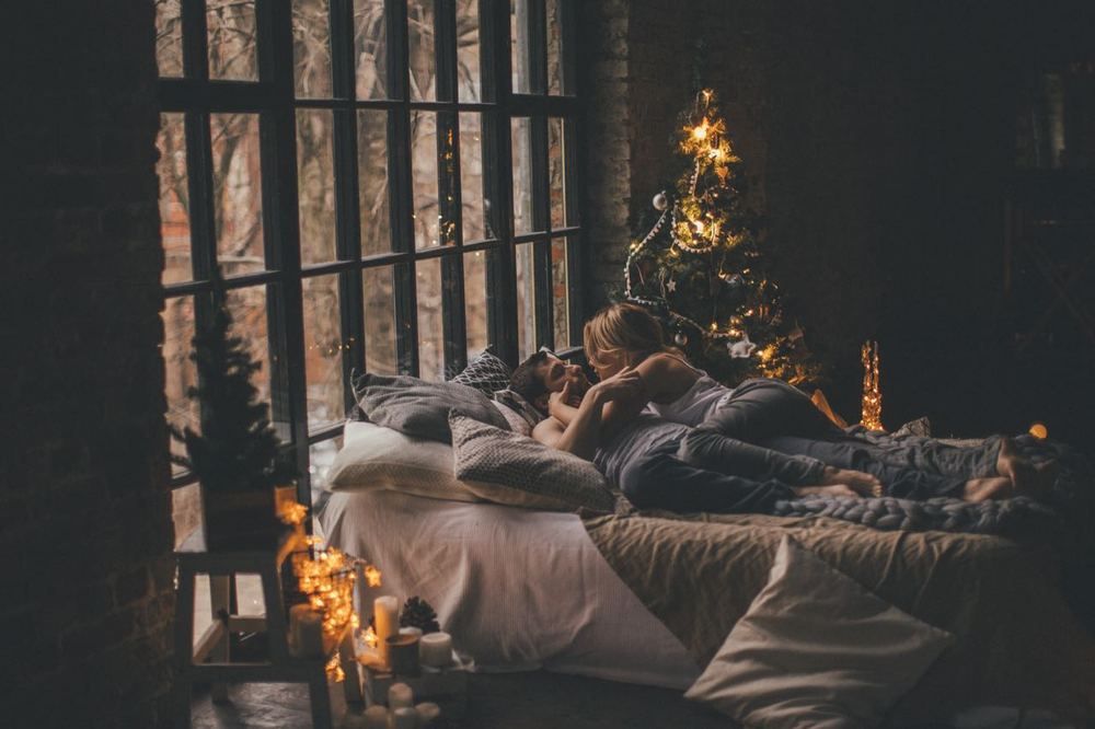 Фото Девушка с парнем лежат на кровати в комнате с новогодней елкой