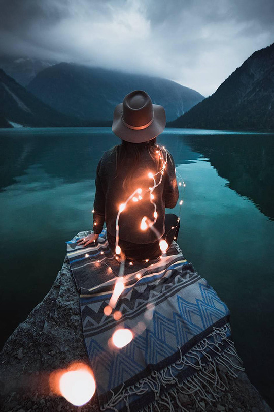 Фото Девушка сидит у озера и держит в руках гирлянду, смотря на горы