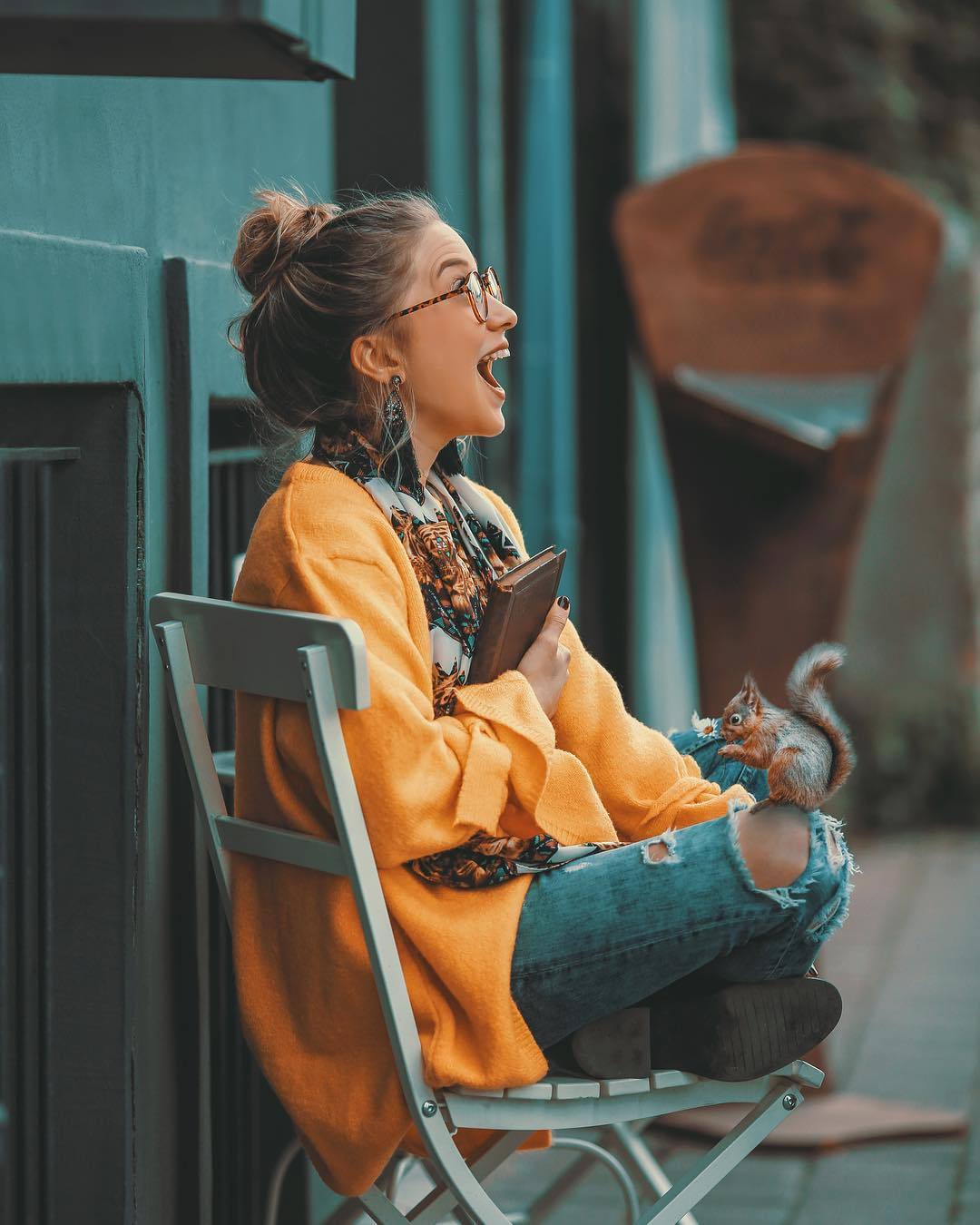 Фото Радостная девушка в очках, в рваных джинсах, на ноге которой сидит белочка с ромашкой, by Zaman Doktoru