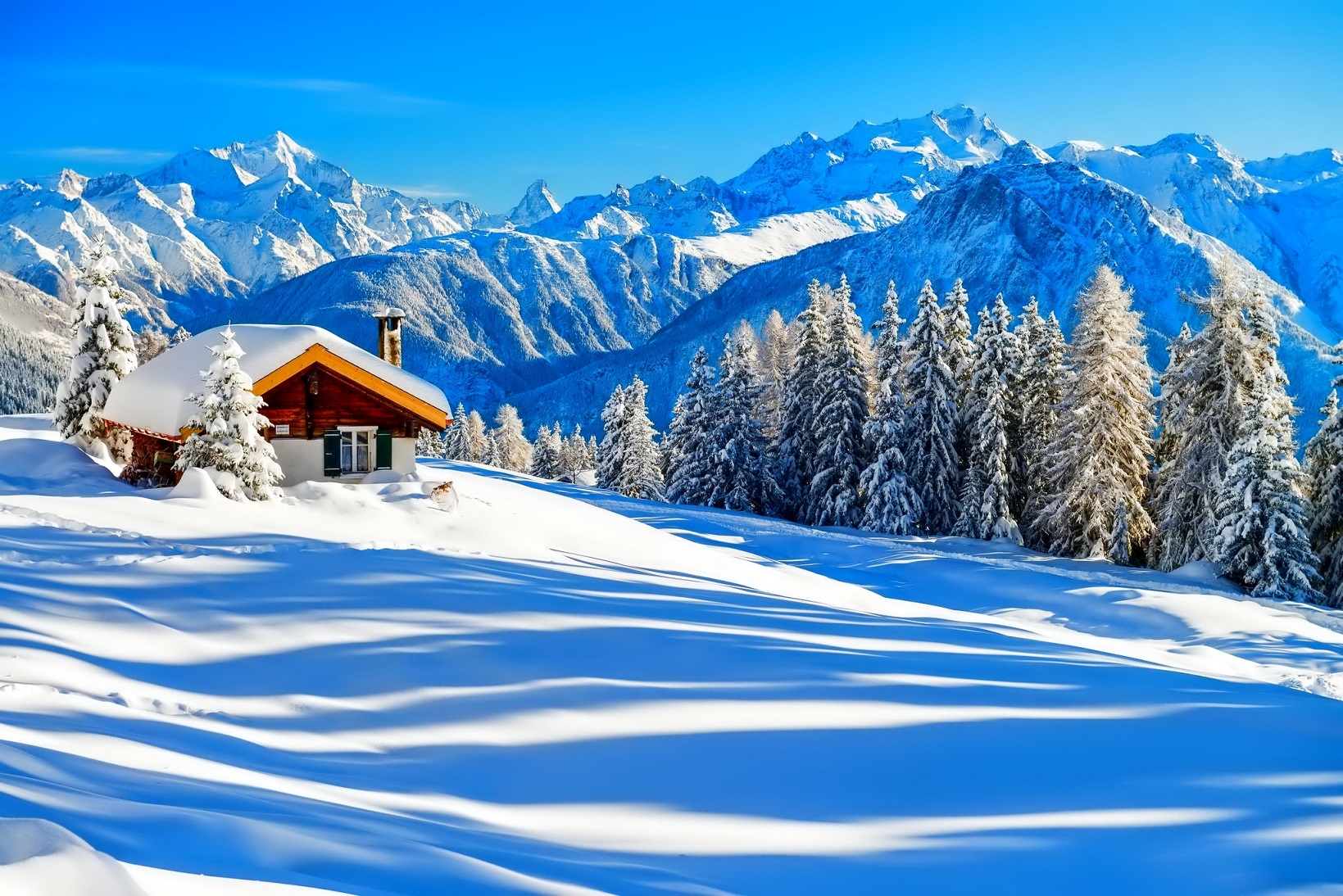 Фото Деревянный домик ясным зимним днем на фоне заснеженных гор