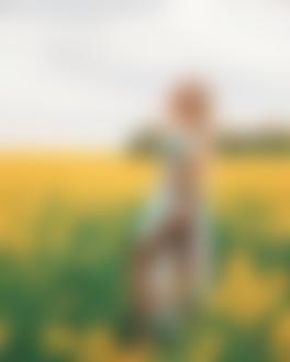 Фото Девушка в платье с оголенной ножкой стоит на цветочном поле