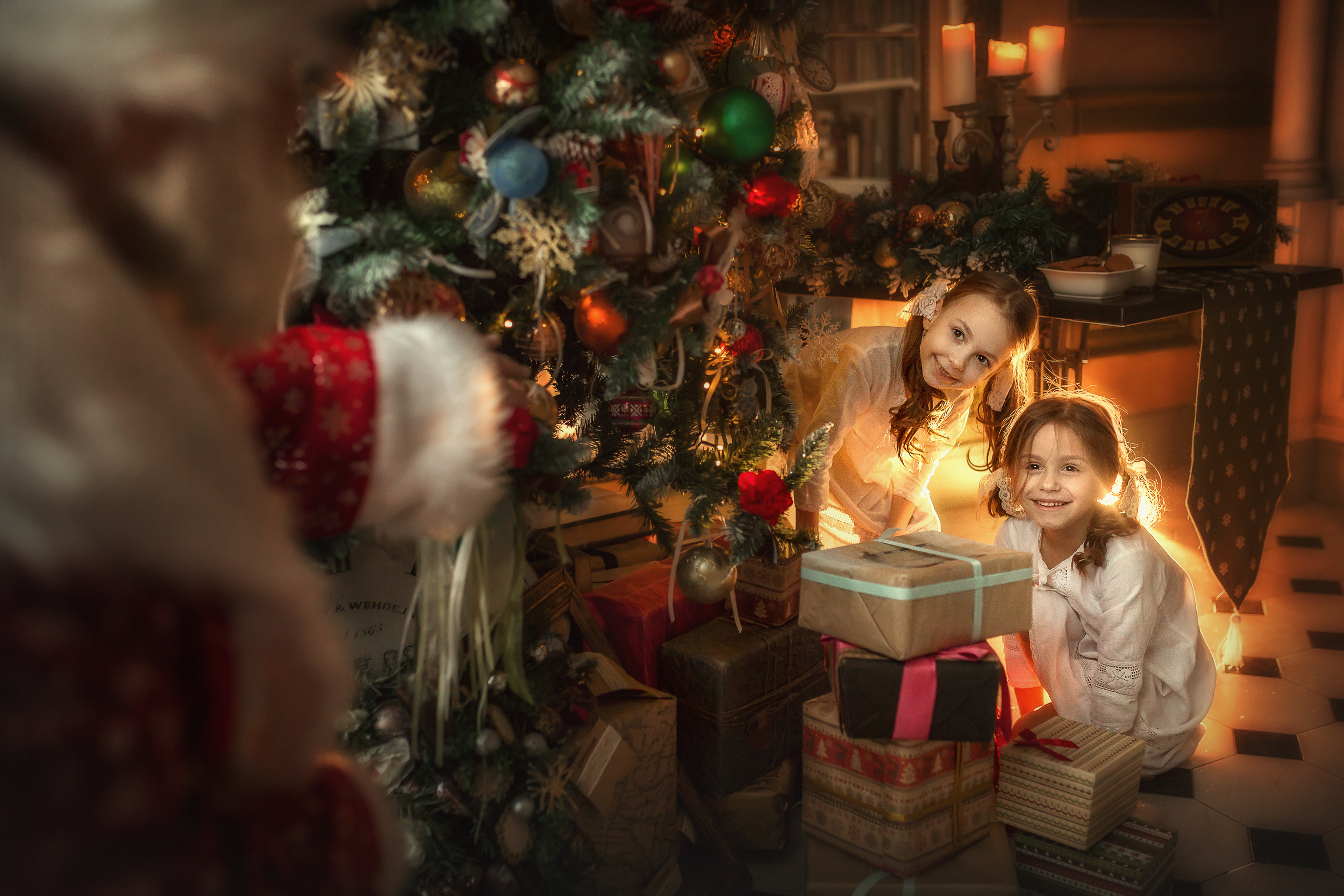 Фото Девочки сидят у подарков под елкой и смотрят на Деда Мороза. Фотограф Савченко Кристина