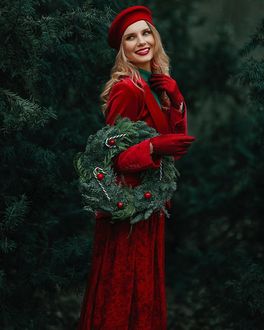 Фото Девушка в красном костюме в берете стоит у елок с новогодним венком на руке, by janinas_photography