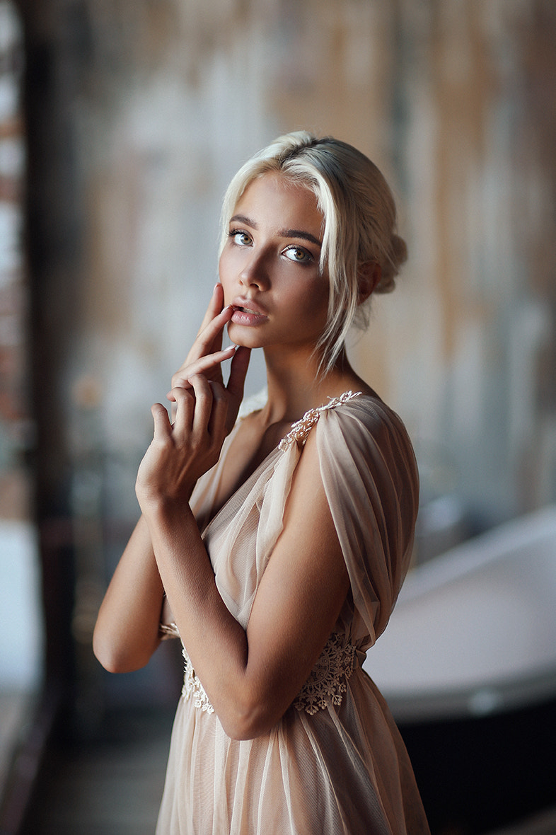 Фото Модель Екатерина Ширяева с белыми волосами в прозрачной туники держит руки у лица фотограф