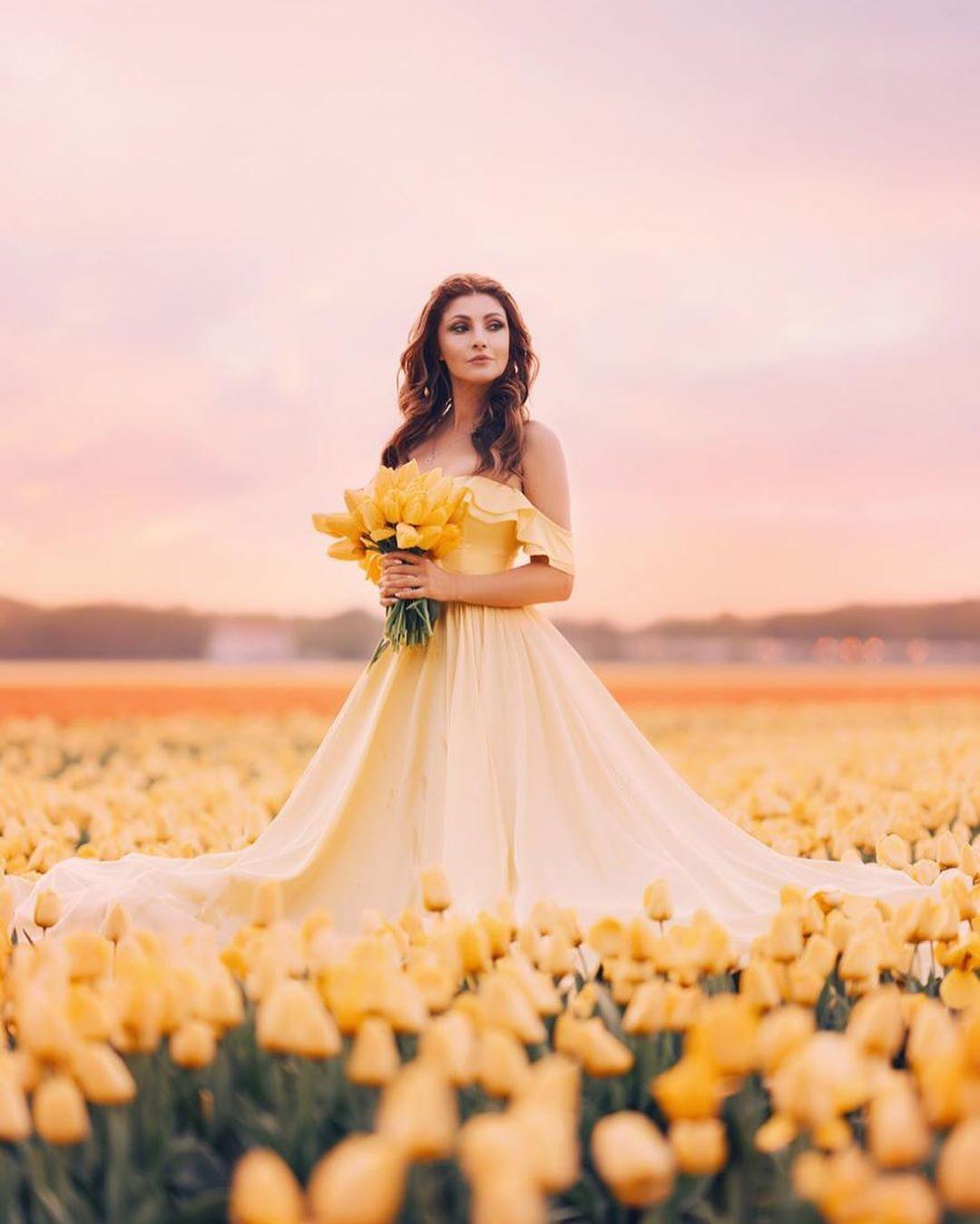 Фото Актриса Анастасия Макеева в длинном платье стоит среди желтых тюльпанов