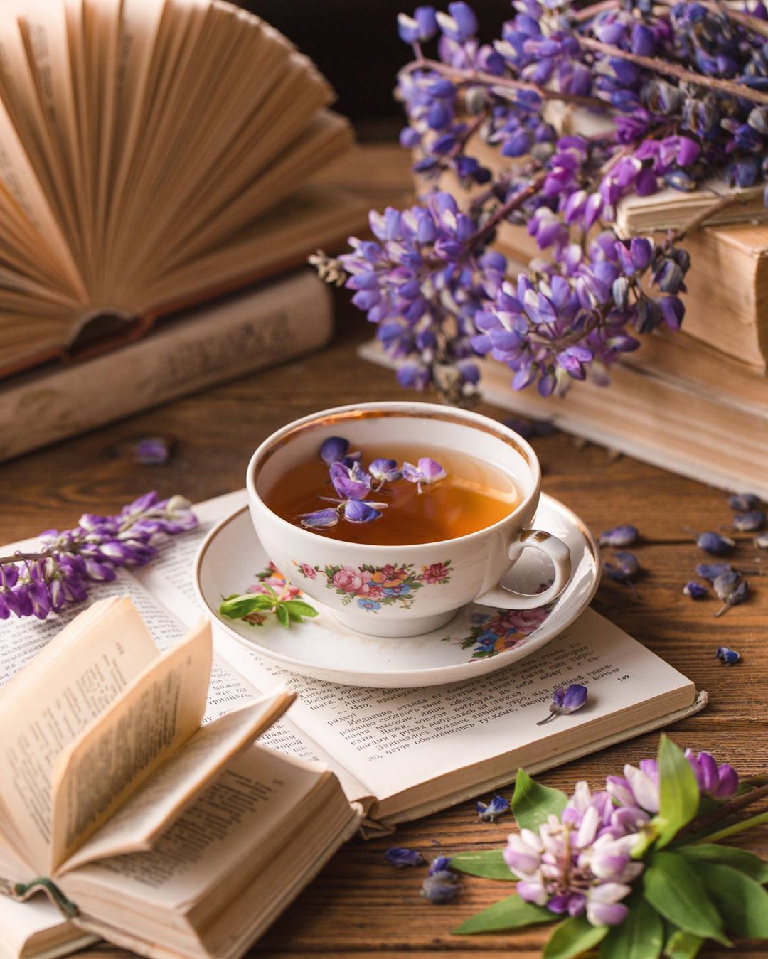 Фото Чашка с чаем на блюдце стоит на открытой книге и рядом цветы глицинии