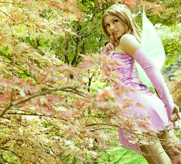 Фото фото косплей персонажа флора / flora из мультфильма винкс / winx club гуляет на улице на природе в лесу среди цветов на деревьях показывая палец у лица
