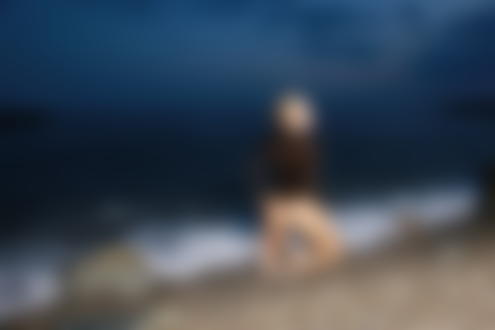 Фото Девушка - блондинка в черном боди стоит на коленках у моря
