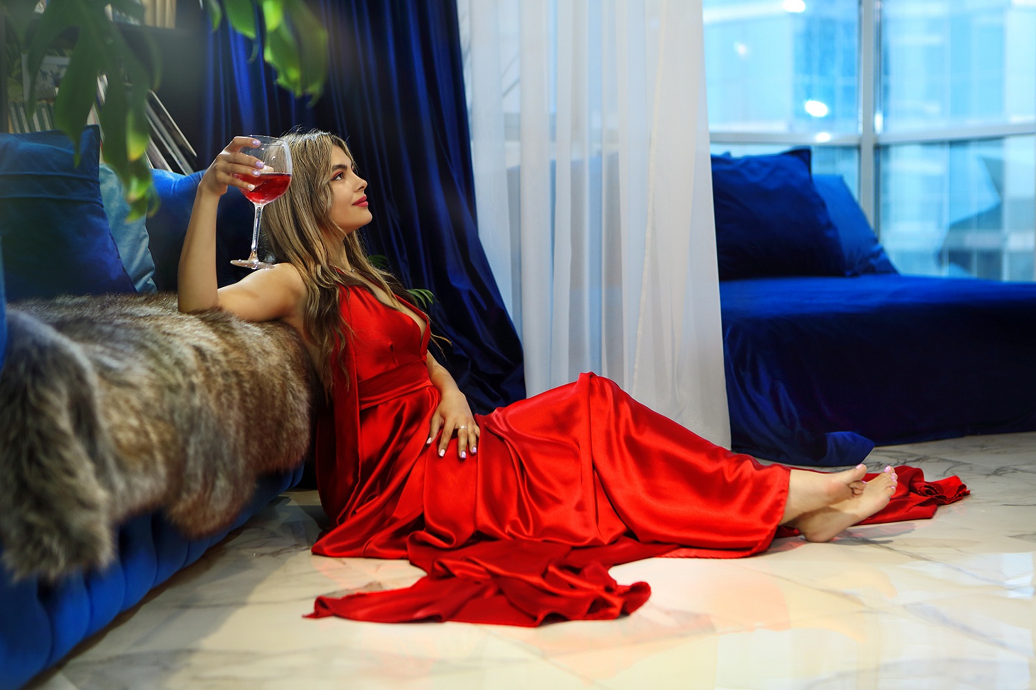 Фото Девушка в красном платье сидит на полу у дивана и держит в руке бокал вина