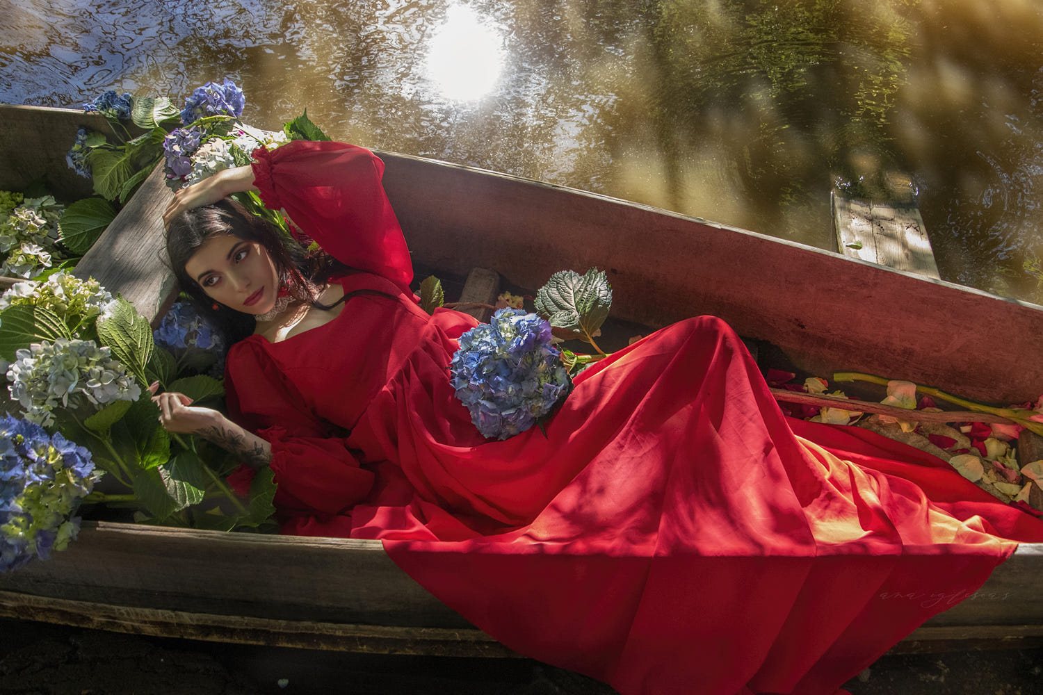 Фото Девушка в длинном красном платье, с голубыми цветами лежит в лодке