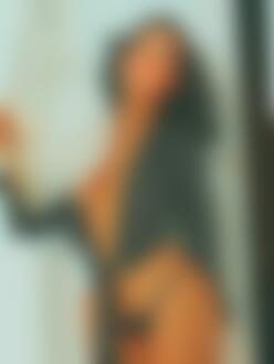 Фото Темноволосая девушка в верхней одежде с принтом горошек и в черном нижнем белье, с веером, стоит в комнате