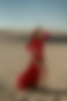 Фото Девушка в длинном красном платье стоит на песке, выставив ножку