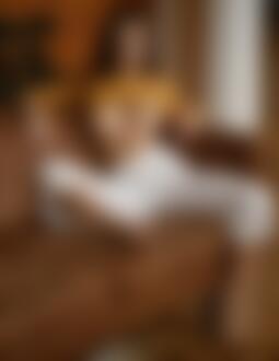 Фото Девушка в приподнятой кофте и белых штанах сидит на диване
