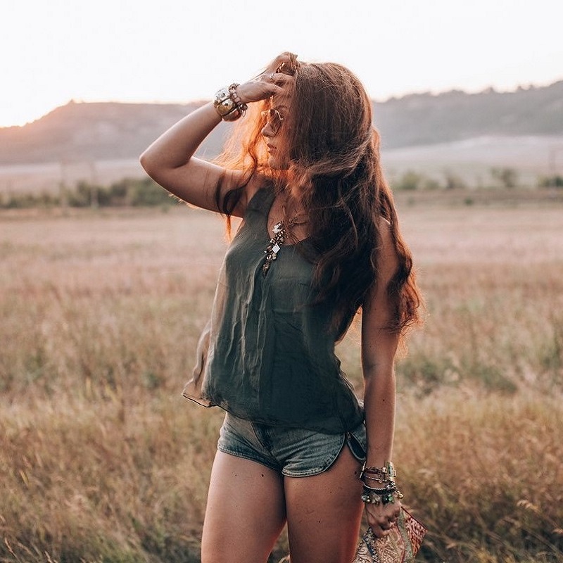 Фото Девушка с длинными волосами в блузке и шортах стоит на поле и смотрит в сторону
