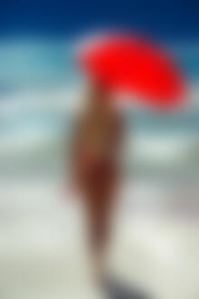 Фото Блондинка с красным зонтом стоит на фоне моря