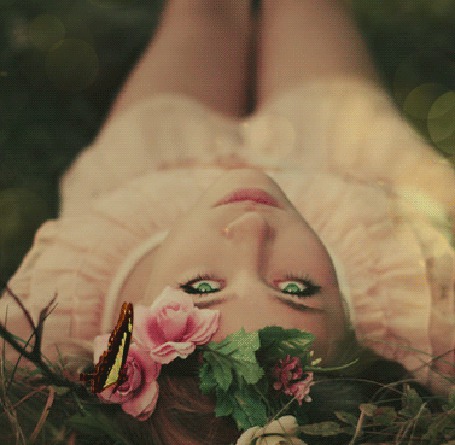 Аанимации Девушка с зелеными глазами лежит в траве на спине, на цветок у нее на голове села бабочка