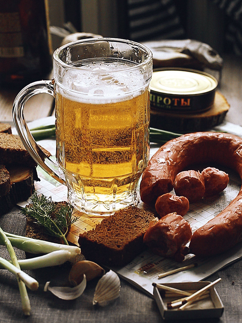 Анимация Традиционно накрытый стол на празднике Лиго: пиво, банка шпрот, ржаной хлеб, копченная колбаса, лук и спички, для того, чтобы разжечь костер, гифка