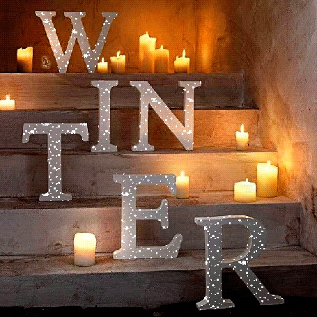 Анимация Переливающиеся буквы слова winter / зима на ступеньках рядом с горящими свечами