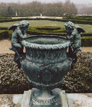 Анимация Хлопья снега пролетают над скульптурой, на которой изображены два ангелы заглядывающие в чашу, на фоне декоративно подстриженного парка