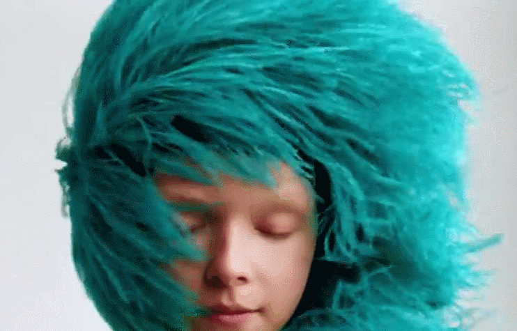 Анимация Улыбчивая девушка в лохматой меховой шапке бирюзового цвета, мех которой колышется нам ветру, гифка Улыбчивая девушка в лохматой меховой шапке бирюзового цвета, мех которой колышется нам ветру