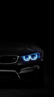 Обои на телефон Фронтальная часть автомобиля BMW 5 серии с яркими голубыми фарами, светящимися в темноте, на черном фоне