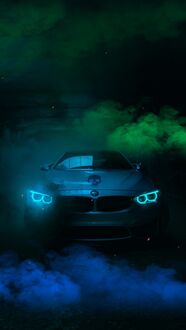 Обои на телефон Серебряный автомобиль BMW M3 с включенными ярко-голубыми фарами стоит на темной поверхности, на фоне синего и зеленого дыма