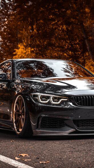 обои на телефон Черный спортивный автомобиль BMW 4-й серии с заниженной подвеской стоит на дороге на фоне осенних деревьев