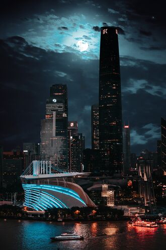 обои на телефон Гуанчжоу / Guanchzhou, Китай / China: современный стадион с синей подсветкой и освещенные небоскребы в ночном городе на фоне темного неба с полной луной и облаками