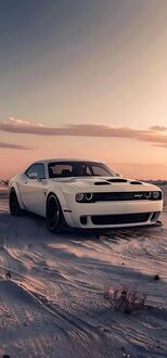 Обои на телефон Белый спортивный автомобиль Dodge Challenger на песчаной поверхности, на фоне неба с розовыми и оранжевыми облаками на закате