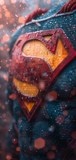 Обои на телефон Эмблема Супермена из фильма Супермен / Superman на его синем костюме, покрытая каплями воды и частицами снега, на фоне размытых оранжевых огней